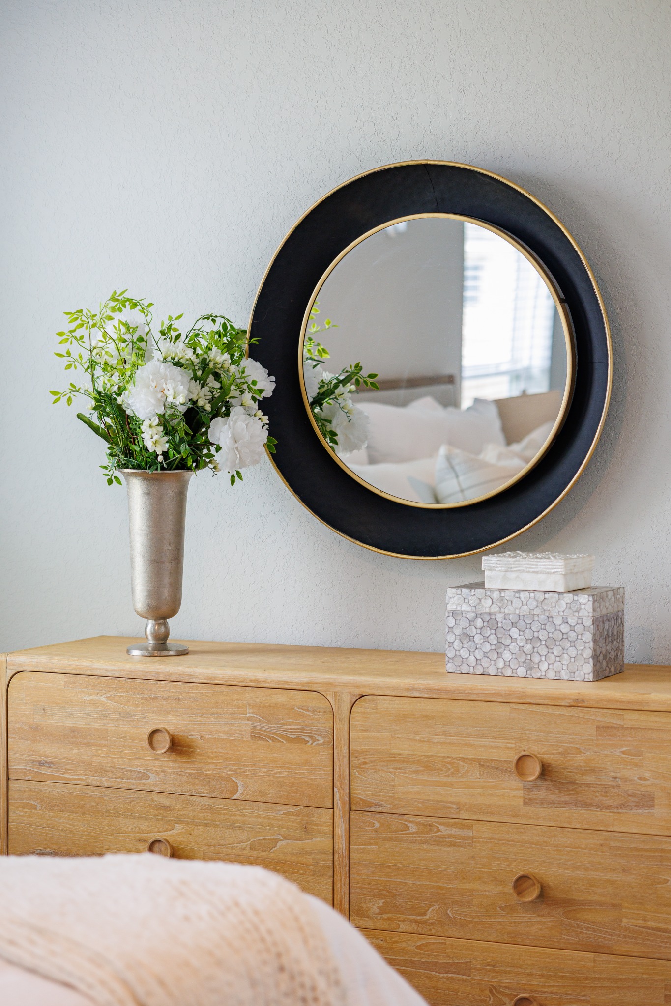 Round mirror and flowers above a wood dresser